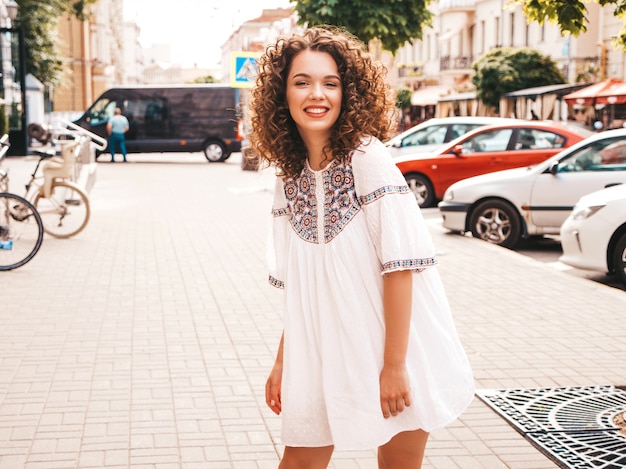 Het portret van mooi het glimlachen model met het kapsel van afrokrullen kleedde zich in de zomer hipster witte kleding.