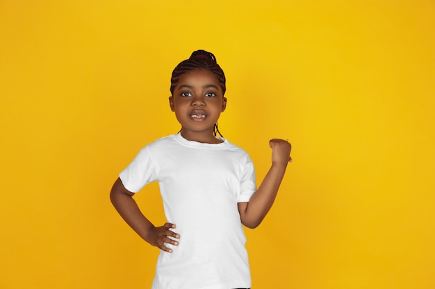 Het portret van weinig Afrikaans-Amerikaans meisje dat op gele studio wordt geïsoleerd