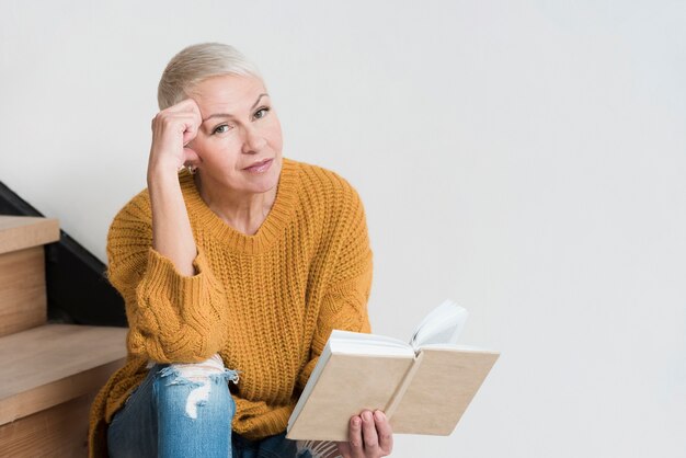 Het rijpe vrouw stellen op treden terwijl het houden van boek