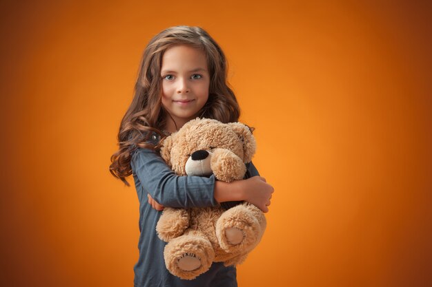 Het schattige vrolijke kleine meisje op een oranje achtergrond