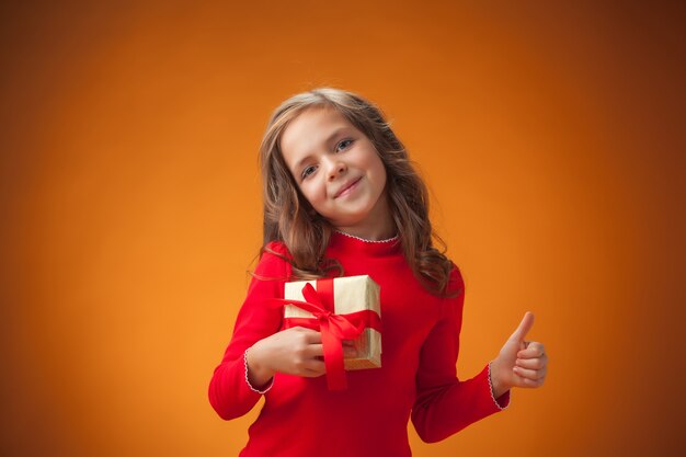 Het schattige vrolijke meisje met cadeau op een oranje achtergrond