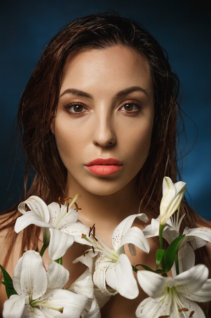 Het schitterende vrouw stellen in witte leliebloemen, die recht kijken.