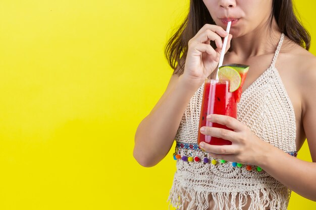 Het sexy meisje drinkt watermalonwater in het hete weer van Sumer met hoed op gele muur.