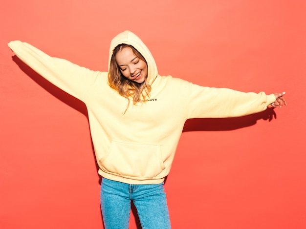 Gratis foto het sexy onbezorgde vrouw stellen dichtbij roze muur. positief model dat pret heeft. het opheffen van haar handen