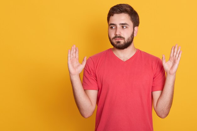 Het studioschot van de ernstige toevallige mens houdt handen omhoog geïsoleerd over geel