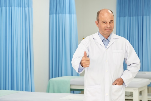 Het succesvolle chiropracticus stellen in het medische bureau tonen beduimelt omhoog