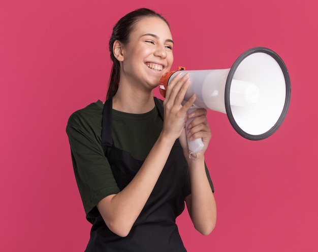 Het tevreden jonge donkerbruine kappermeisje in uniform houdt luide spreker die kant op roze bekijkt