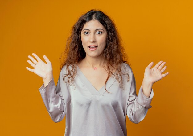 Het tevreden jonge mooie meisje spreidt handen uit die op gele muur worden geïsoleerd