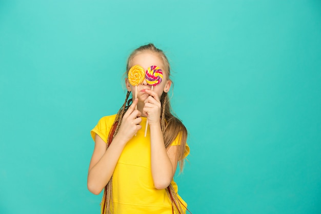 Het tienermeisje met kleurrijke lolly op een blauwe muur