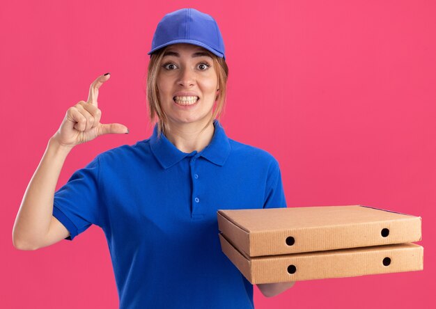 Het verbaasde jonge mooie bezorgmeisje in uniform met pizzadozen doet alsof ze iets op roze vasthoudt