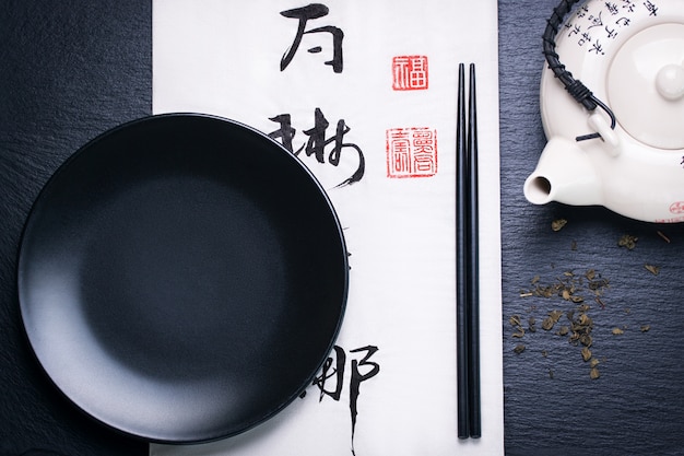 Het voedsel van Azië samenstelling met Chinese stokjes en lege plaat op een donkere steen achtergrond