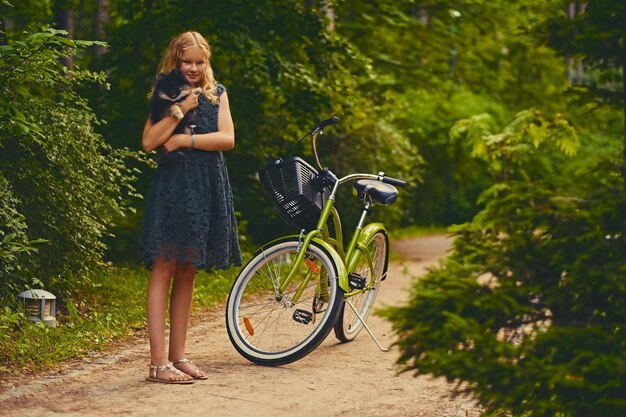 Het volledige lichaamsbeeld van blond meisje houdt Spitz-hond over fietsachtergrond.