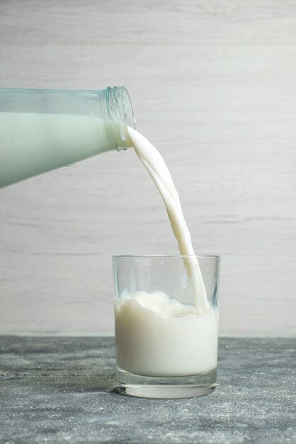 Het vooraanzicht het gieten melk in het kleine glas op wit, drinkt melkfabriek melkproduct