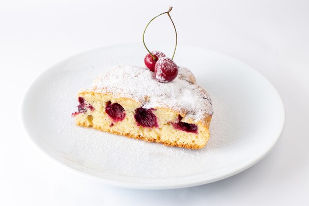 Het vooraanzicht van de plak van de kersencake binnen plaat met suikerpoeder op het witte deeg van de het koekjes zoete suiker van de oppervlaktecake bakt