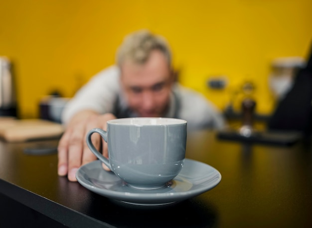 Het vooraanzicht van defocused barista bekijkend kop van koffie