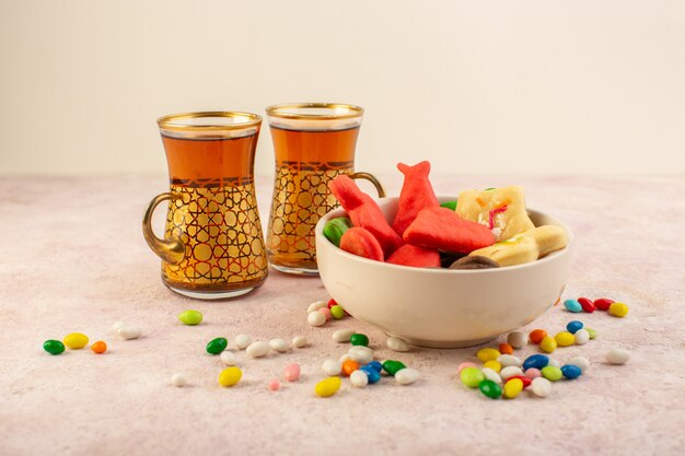 Het vooraanzicht van kleurrijke heerlijke koekjes vormde verschillend binnen plaat met suikergoed en kop theeën