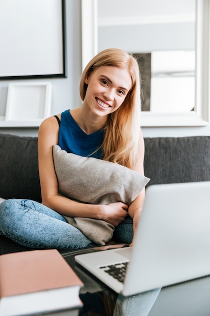 Het vrolijke hoofdkussen van de vrouwenholding en het gebruiken van laptop op bank