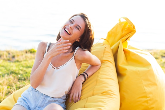 Het vrolijke vrouw stellen op gele beanbag