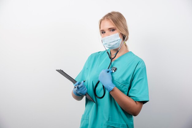 Het vrouwelijke Klembord van de artsenholding en het dragen van een medisch masker. Hoge kwaliteit foto