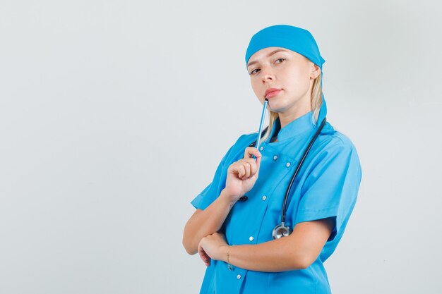 Het vrouwelijke potlood van de artsenholding dichtbij mond in blauw uniform en kijkt ernstig