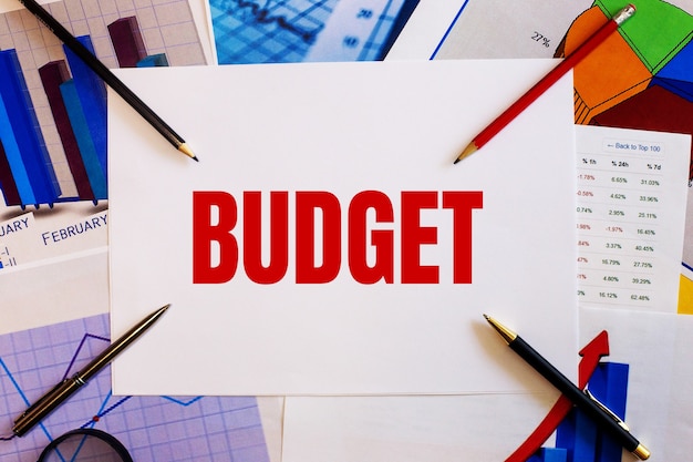 Het woord budget is geschreven op een witte muur in de buurt van gekleurde grafieken, pennen en potloden. bedrijfsconcept