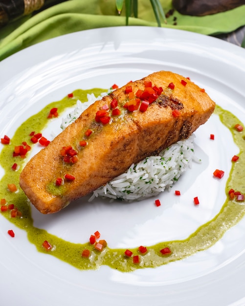 Het zijaanzicht roosterde visfilet met rijst versiert saus en Spaanse peperpeper op een plaat