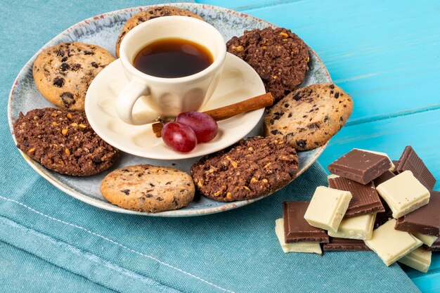 Het zijaanzicht van een kop van koffie diende met havermeelkoekjes en chocolade op blauwe achtergrond