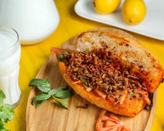 Het zijaanzicht van gehakt met groenten in brood diende met verse tomaten en citroen op houten raad