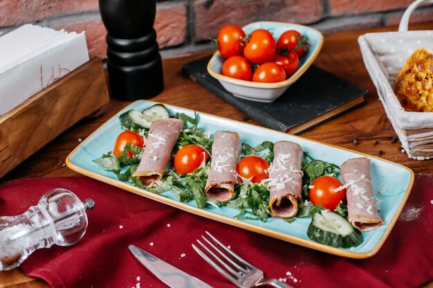 Het zijaanzicht van ham rolt withj tomaten en komkommers op een plaat