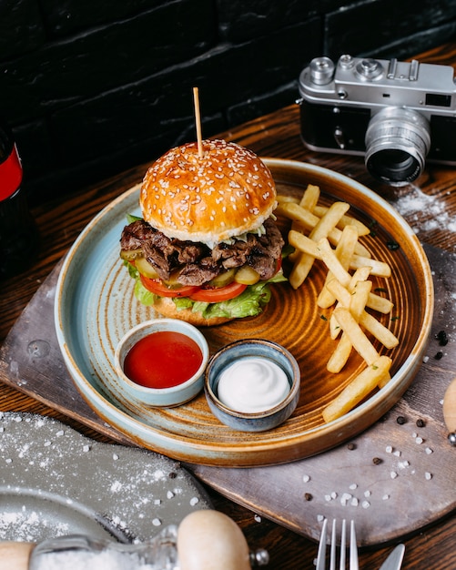 Het zijaanzicht van hamburger met de groenten in het zuur van het rundvlees en tomaten diende met frieten en sauzen op zwarte