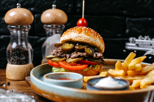 Het zijaanzicht van hamburger met de groenten in het zuur van het rundvlees en tomaten diende met frieten en sauzen op zwarte