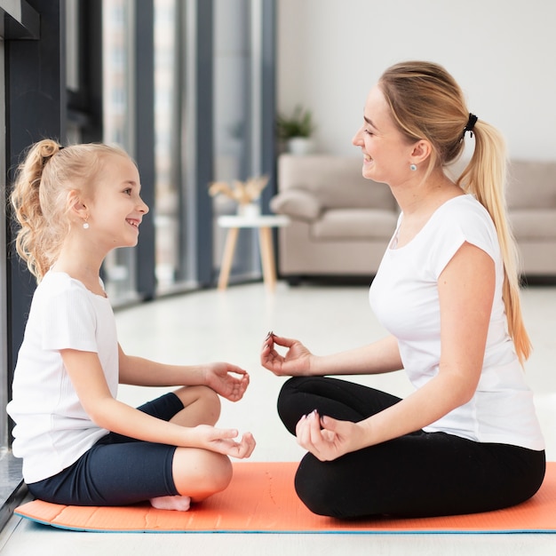 Het zijaanzicht van moeder en dochter die een yoga doen stelt thuis