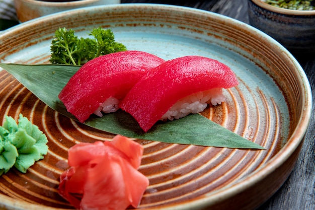 Het zijaanzicht van nigirisushi met tonijn op bamboeblad diende met ingelegde gemberplakken en wasabi op een plaat