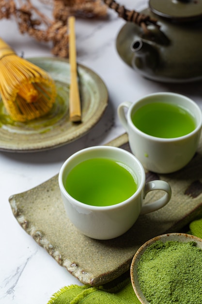 Hete groene thee in een glas met room gegarneerd met groene thee, gedecoreerd met groene theepoeder.