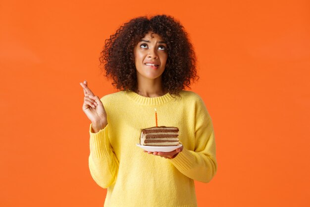 Heupportret hoopvol schattig dromerig, feestvarken met afro-kapsel, bijtende lip en wenswens die uitkomt, hemel biddend opzoeken, veel geluk met de vingers, kaars uitblazen op verjaardagstaart