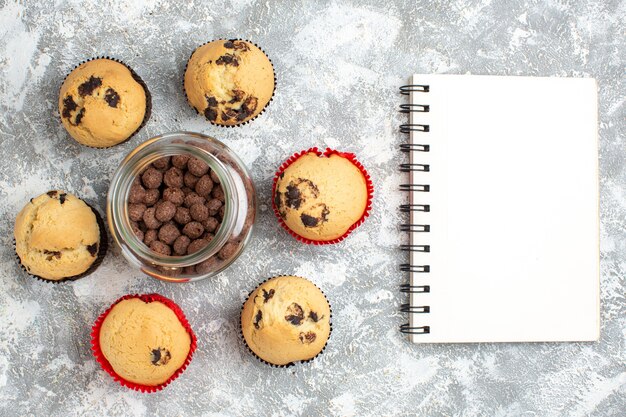 Hierboven heerlijke kleine cupcakes rond chocoladekoekjes in een glazen pot naast notitieboekje op ijsoppervlak