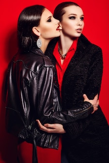 High fashion look.glamor close-up portret van twee mooie sexy stijlvolle brunettes blanke jonge vrouwen modellen in zwarte jas met lichte make-up, met rode lippen, met perfecte schone huid in studio