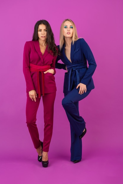 High fashion stijl twee aantrekkelijke vrouwen op violette muur in stijlvolle kleurrijke avondpakken van paarse en blauwe kleur, vrienden samen plezier hebben, modetrend