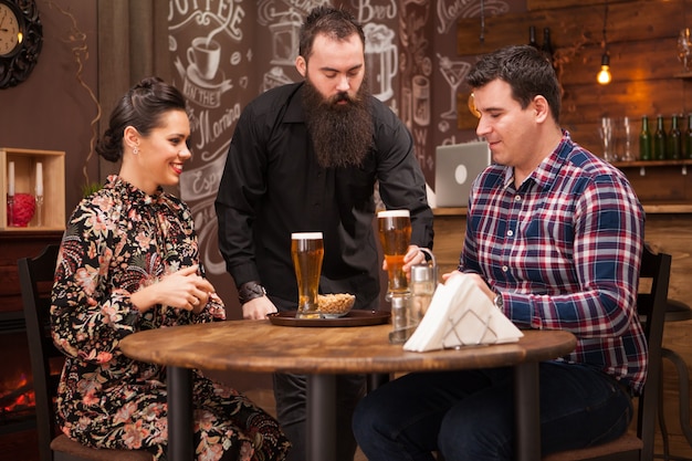 Hipster-barman die de bestelling geeft aan een mooi jong stel. Geweldige pub.