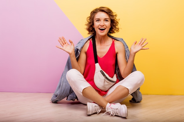 Hipstervrouw met verrassingsgezicht het stellen in studio op roze en geel.