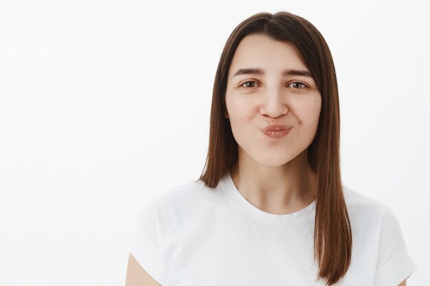 Hmm klinkt lekker. Portret van vrolijk en opgewonden blij jong meisje dat lippen vouwt en glimlacht als kijkend met verlangen, probeer het geamuseerd en geïnteresseerd te staan over grijze muur