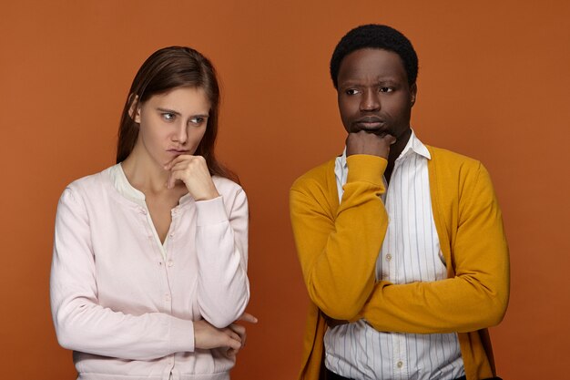 Hmm. Portret van doordachte jonge blanke vrouw met lang haar en haar peinzende donkere mannelijke collega ontwikkelt creatieve ideeën voor startprojecten, diep in gedachten uitdrukkingen