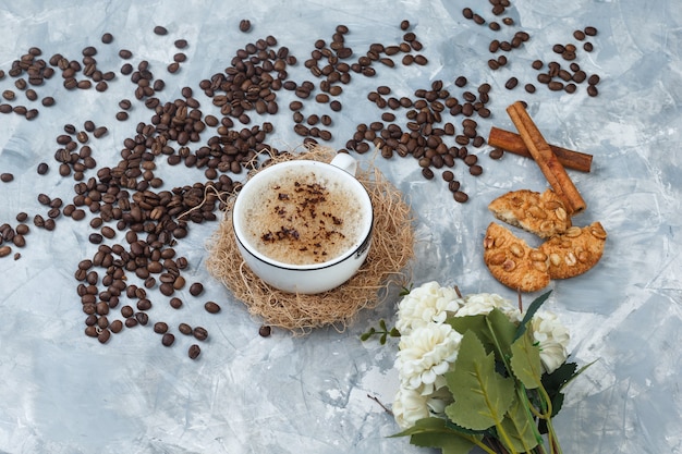 Hoge hoek bekijken koffie in beker met koekjes, koffiebonen, bloemen, kaneelstokjes op grijze gips achtergrond. horizontaal