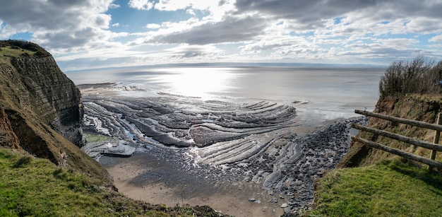 Gratis foto hoge hoek die van een prachtige kust onder de heuvels en de bewolkte hemel op de achtergrond is ontsproten