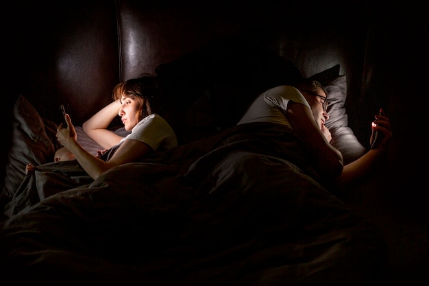 Hoge hoek mensen in bed met smartphones