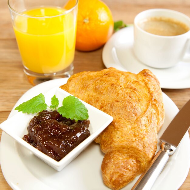 Hoge hoek opname van een heerlijke croissant met jam op een bord, verse jus d'orange en een kopje koffie