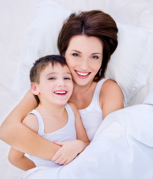 Hoge hoek portret van een lachende jonge moeder en haar mooie zoon liggend op een bed