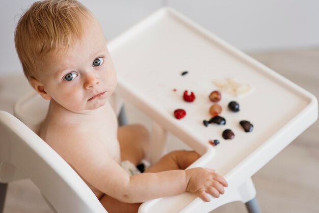 Hoge hoek schattige baby in kinderstoel kiezen welk fruit te eten