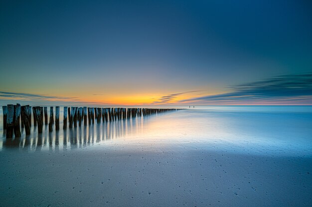 Hoge hoek shot van een houten dek aan de kust die leidt naar de zee bij zonsondergang