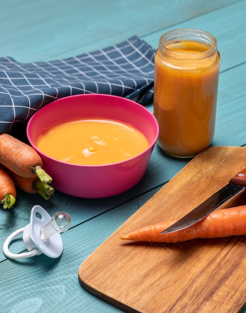 Hoge hoek van babyvoeding in kom met fopspeen en wortelen